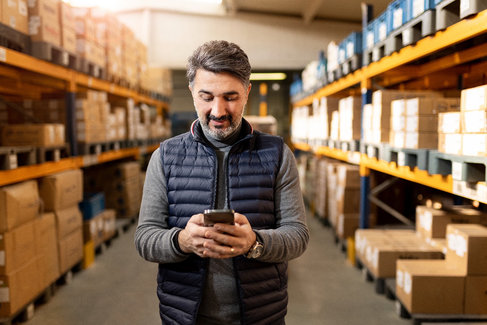 a man in a vest holding a phone in a warehouse