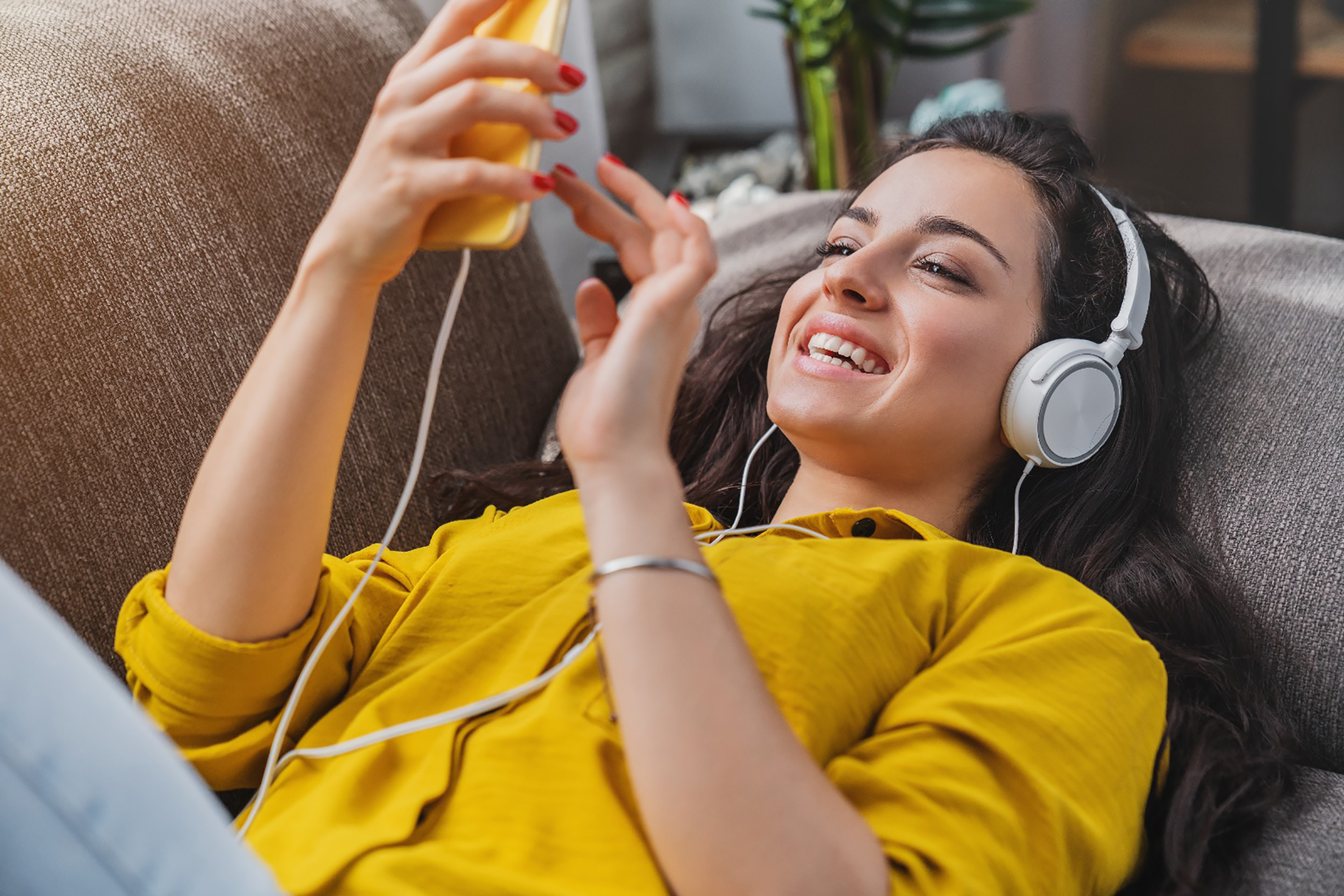 a woman lying on a couch wearing headphones and smiling